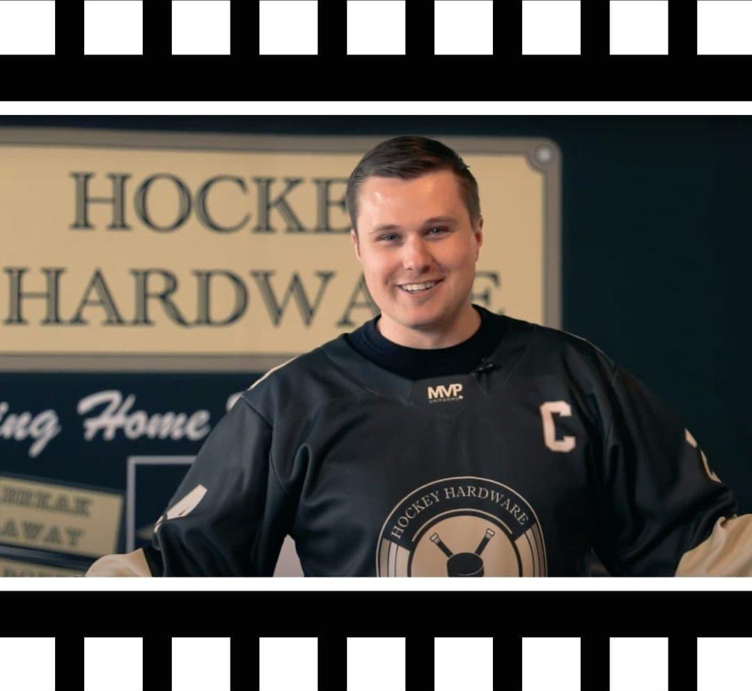 Hockey Hardware creator and FACE-OFF GAMES owner Billy Morrison is smiling and wearing his Hockey Hardware jersey in front of a Hockey Hardware backdrop.