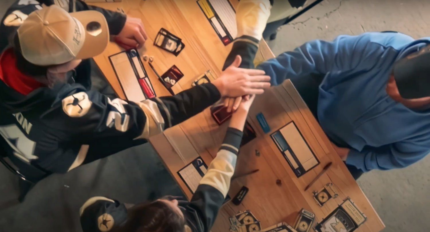 Each player playing Hockey Hardware stretches one arm out in the middle of the table and each player stacks their hands on another.